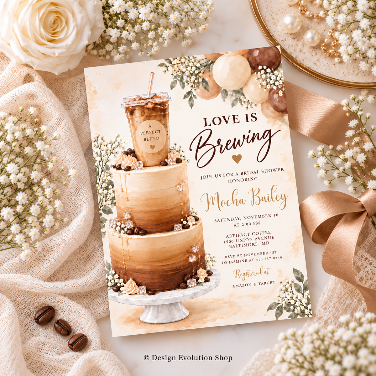 A styled flat-lay of a bridal shower invitation card featuring a three-tier coffee cake illustration and the text 'Love is Brewing.' The card is surrounded by cream roses, baby's breath, coffee beans, a satin ribbon, and a pearl-covered dish on a neutral fabric background.